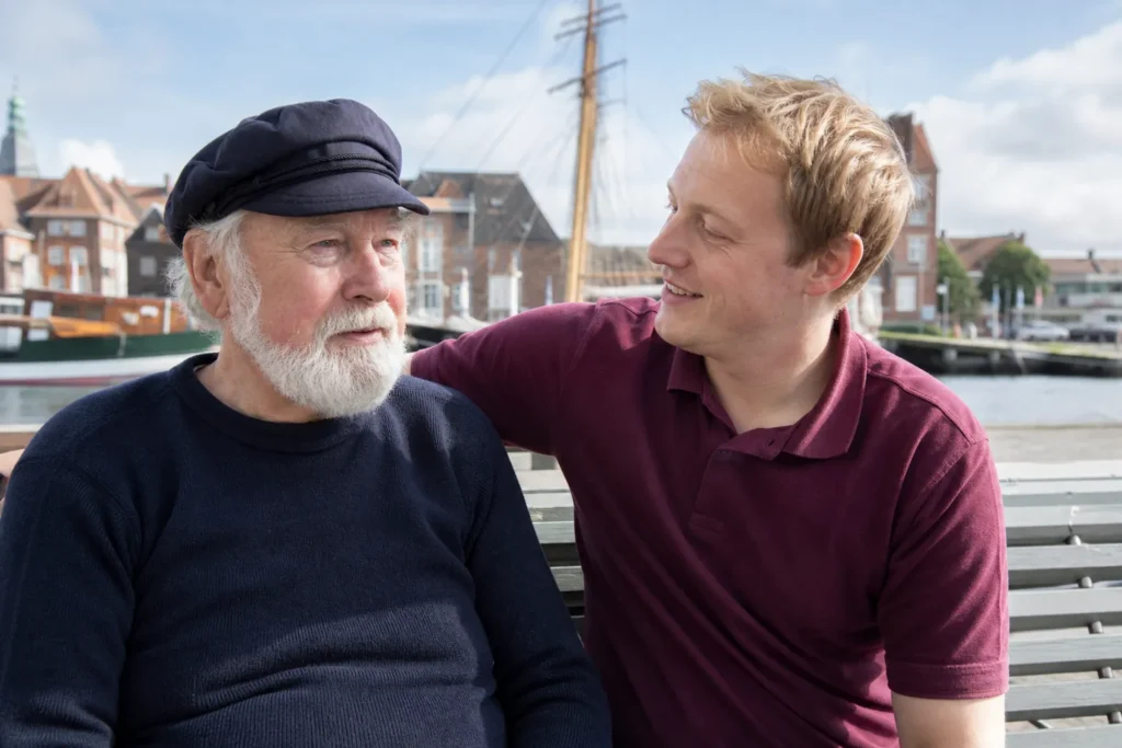 Senior und Betreuer sitzen auf einer Bank am Hafen