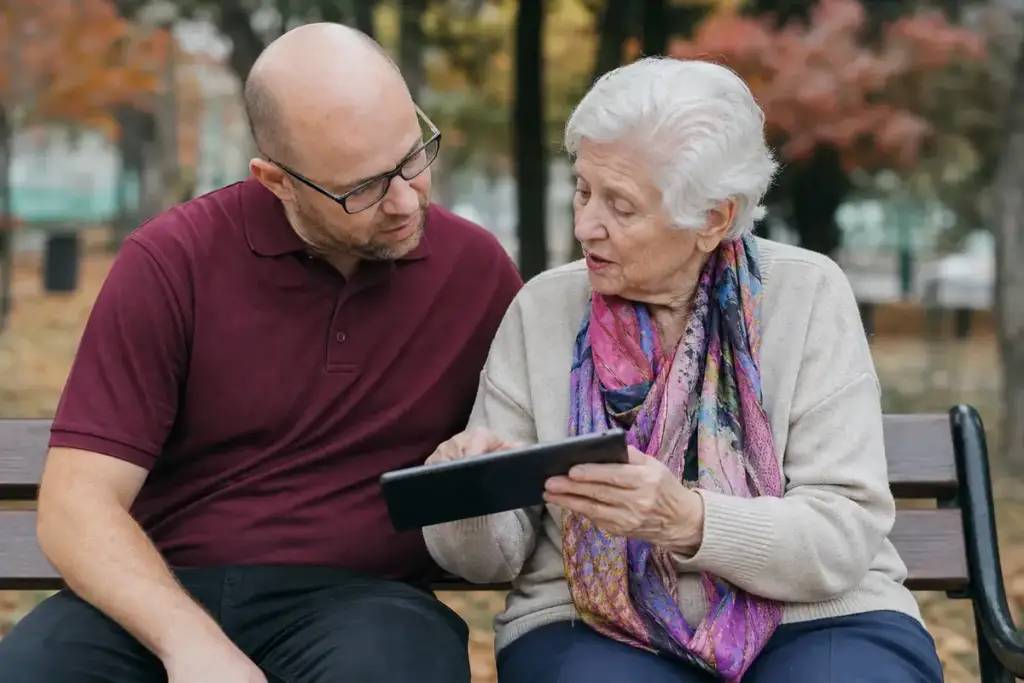 Betreuer hört einer Seniorin zu, die ihm alte Fotos auf dem Tablet zeigt